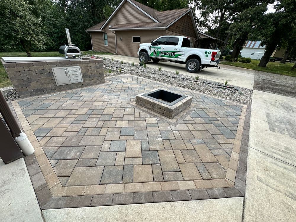Paved outdoor patio with fire pit, outdoor kitchen, and truck in residential setting.