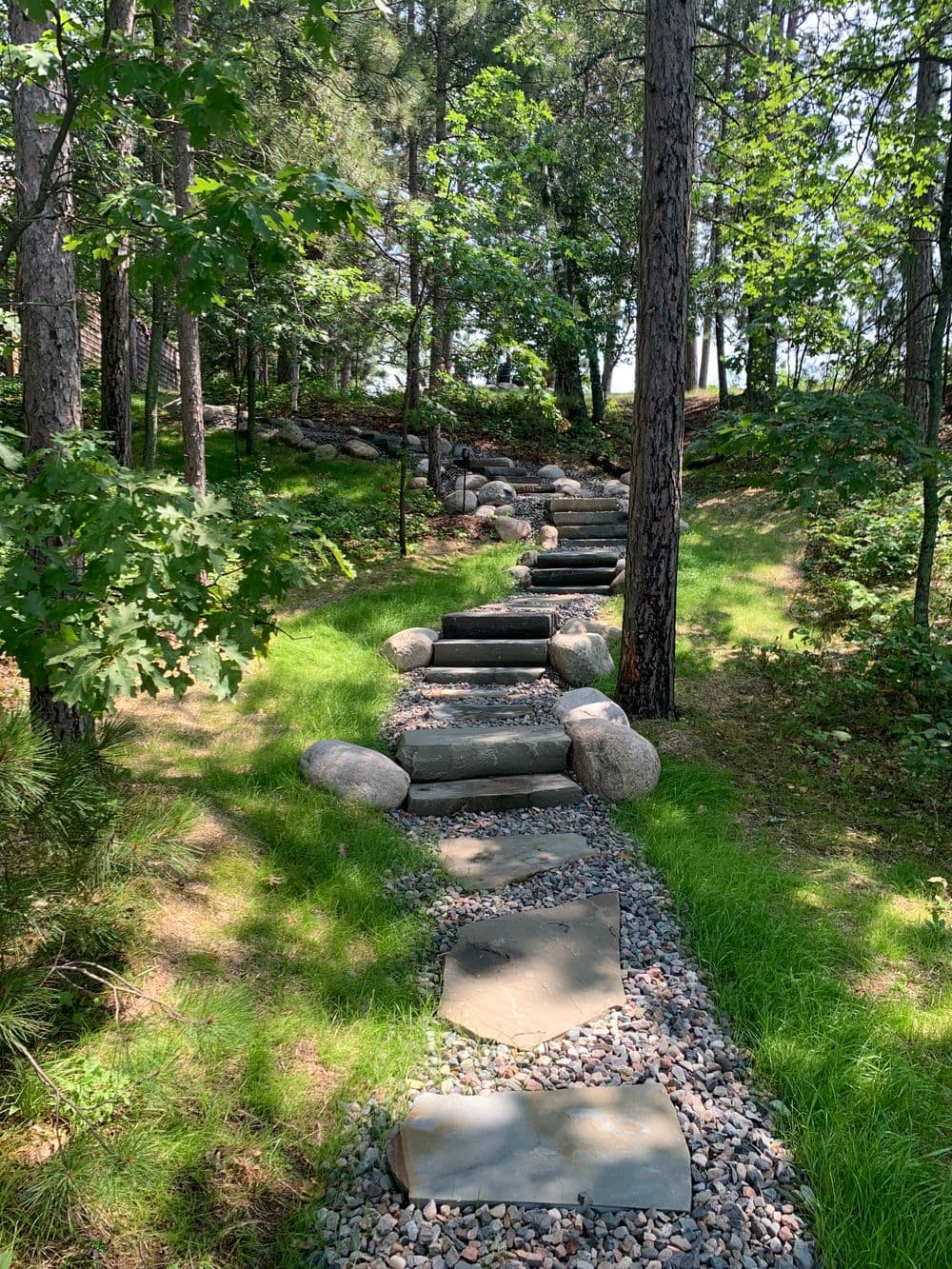 Stone pathway through a lush green forest, lined with rocks and trees.