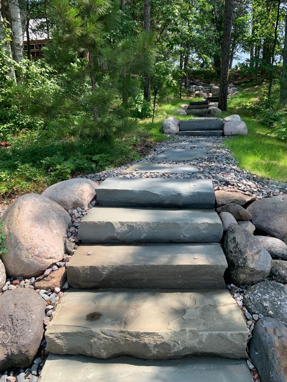 Stone steps leading through a landscaped garden with rocks and greenery.