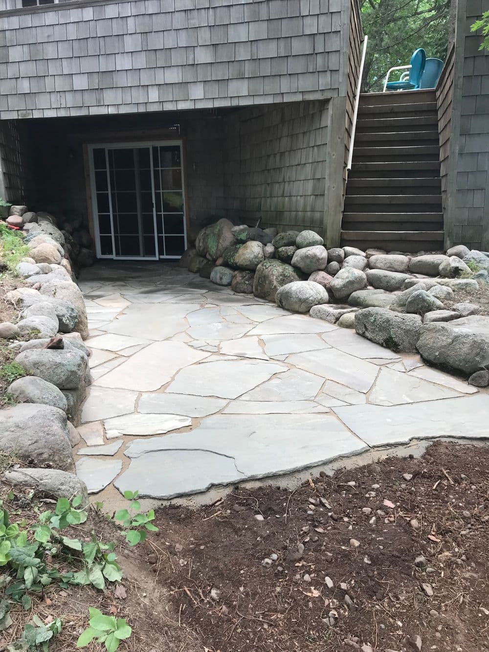 Flagstone pathway with smooth rocks leading to a basement entry under a wooden deck.
