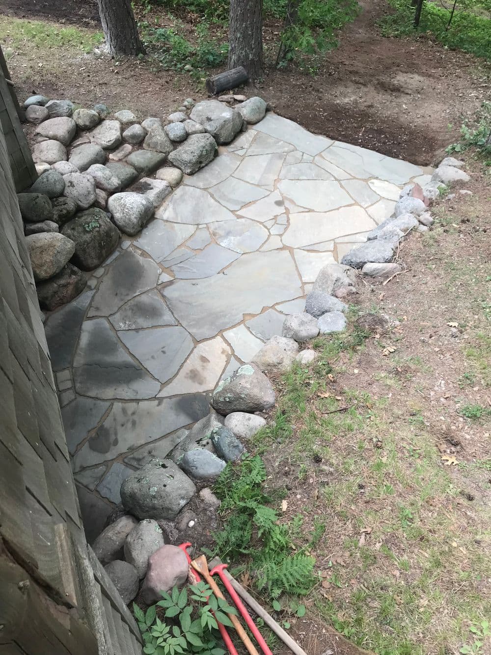 Flagstone patio with stone border, surrounded by greenery and gravel pathway.