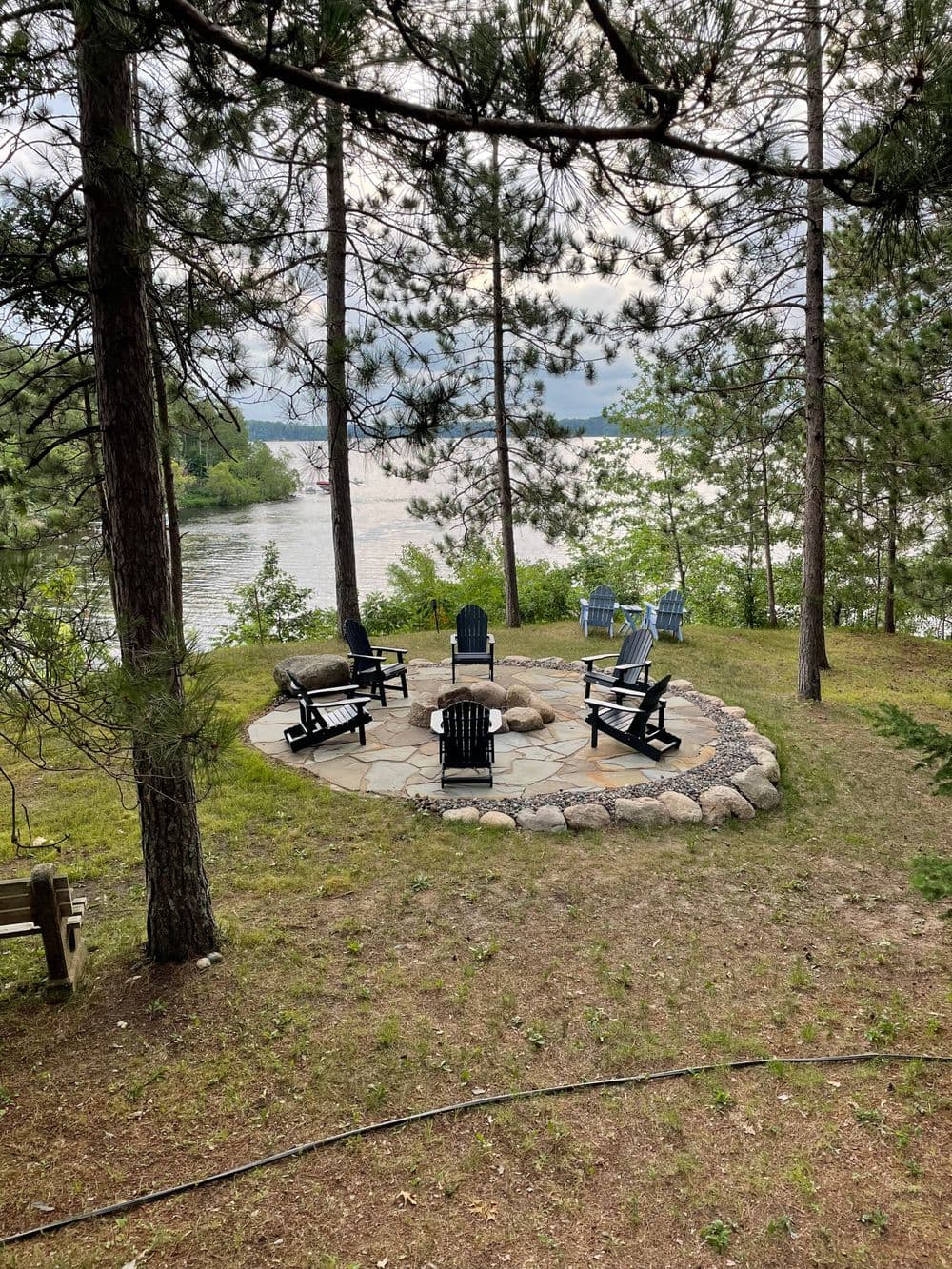 Lakeside seating area with stone patio and chairs surrounded by trees.