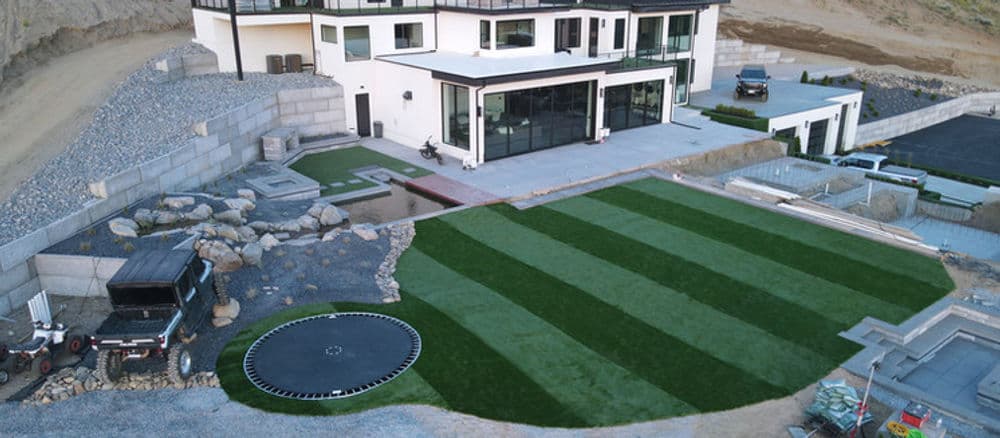 Aerial view of a modern home with manicured lawn, trampoline, and landscaping in progress.
