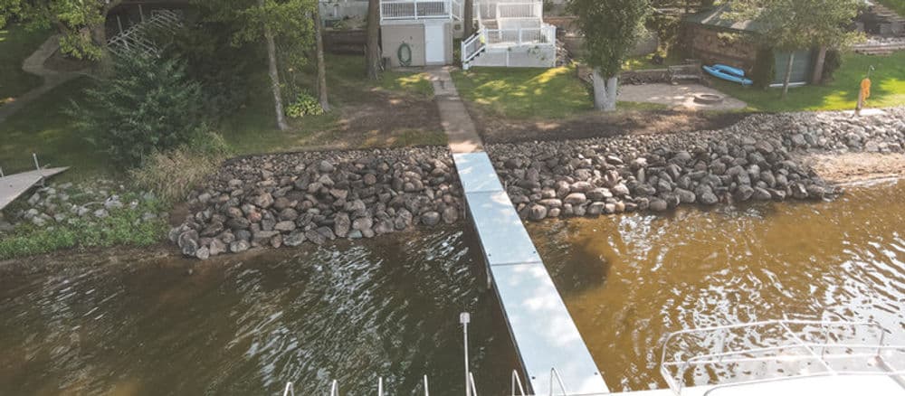 Aerial view of a dock leading to a lake, surrounded by trees and houses.