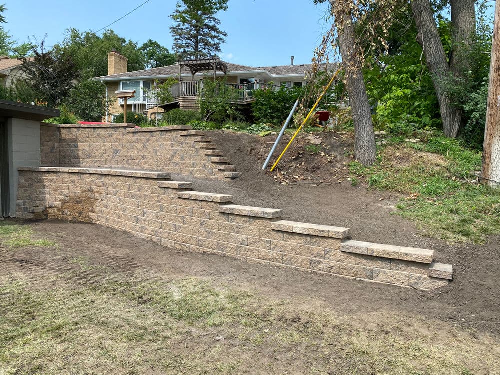 Landscaped yard featuring a stone retaining wall and steps leading to a house in the background.