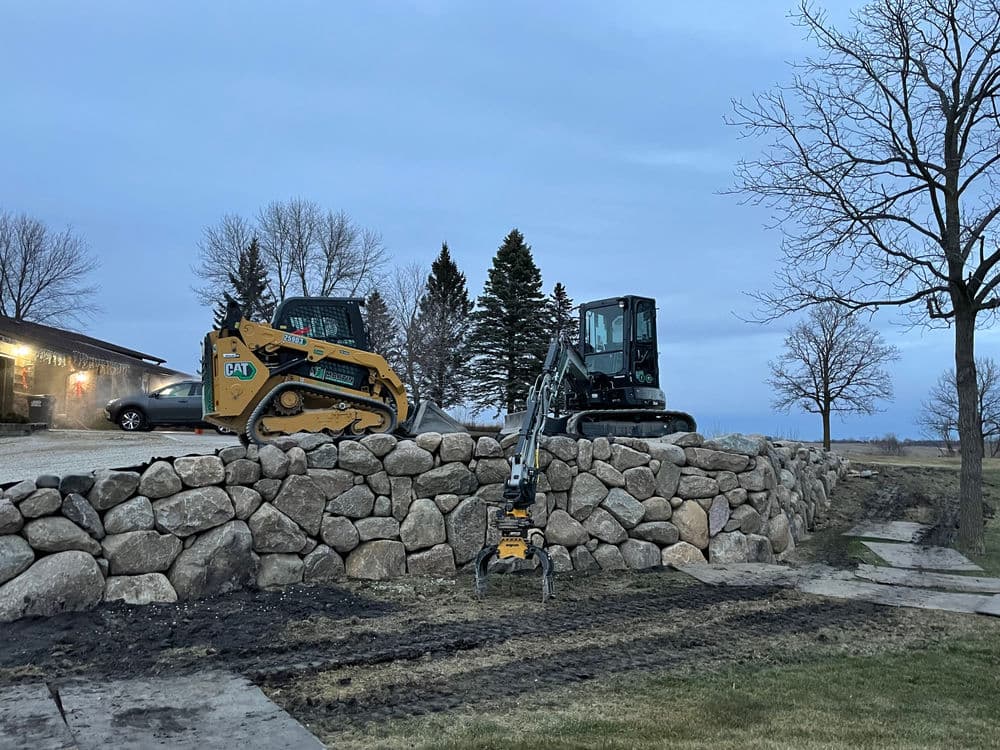 Excavation equipment on rocky landscape during twilight, featuring a skid steer and mini excavator.