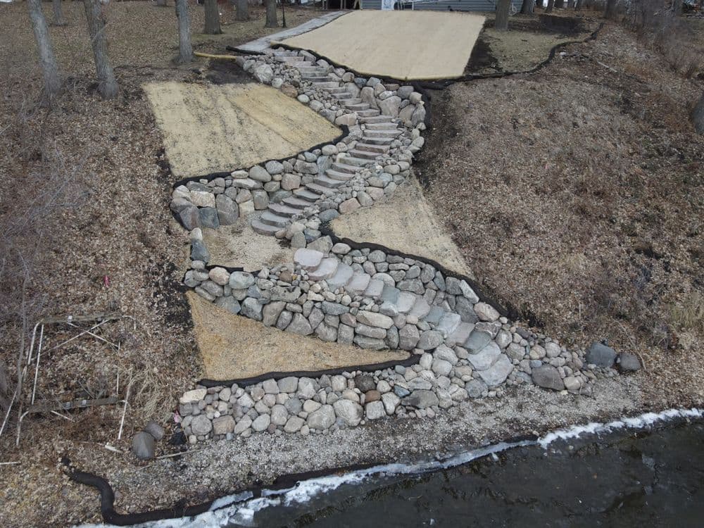Winding stone pathway leading to a river, bordered by grass and landscaped stones.