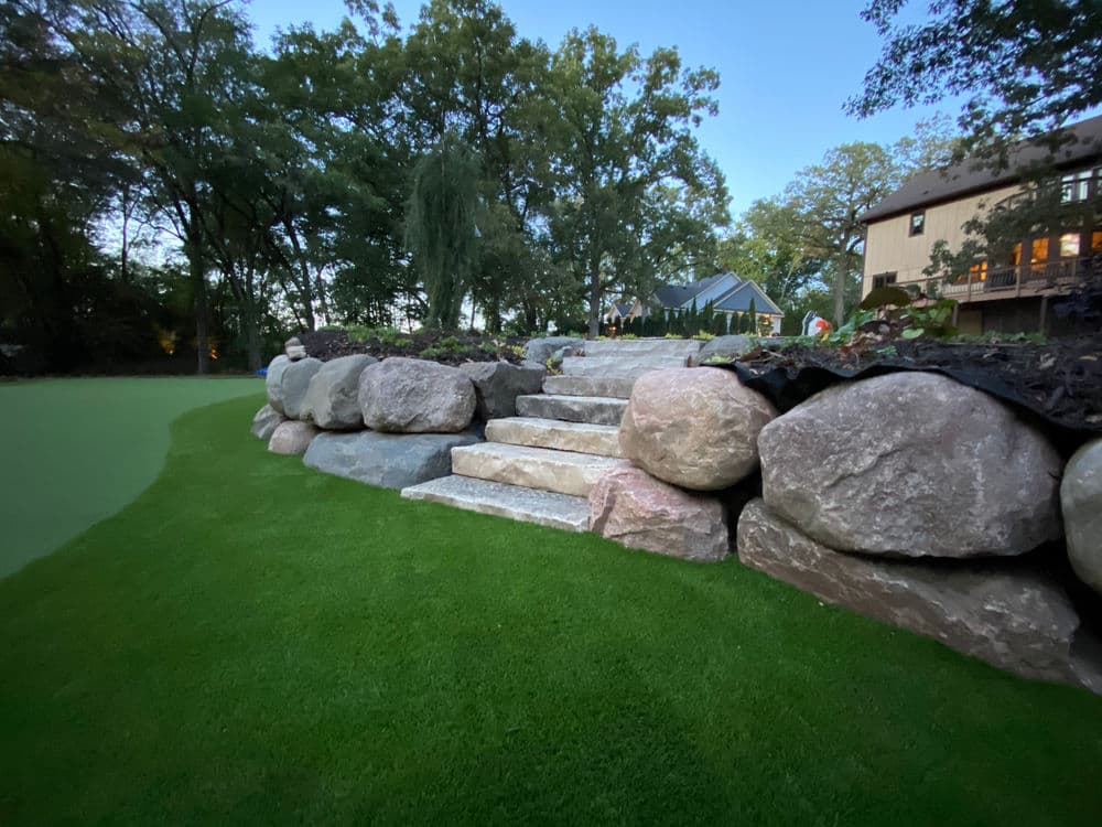 Stone steps leading to a garden area surrounded by greenery and rocks in the evening light.