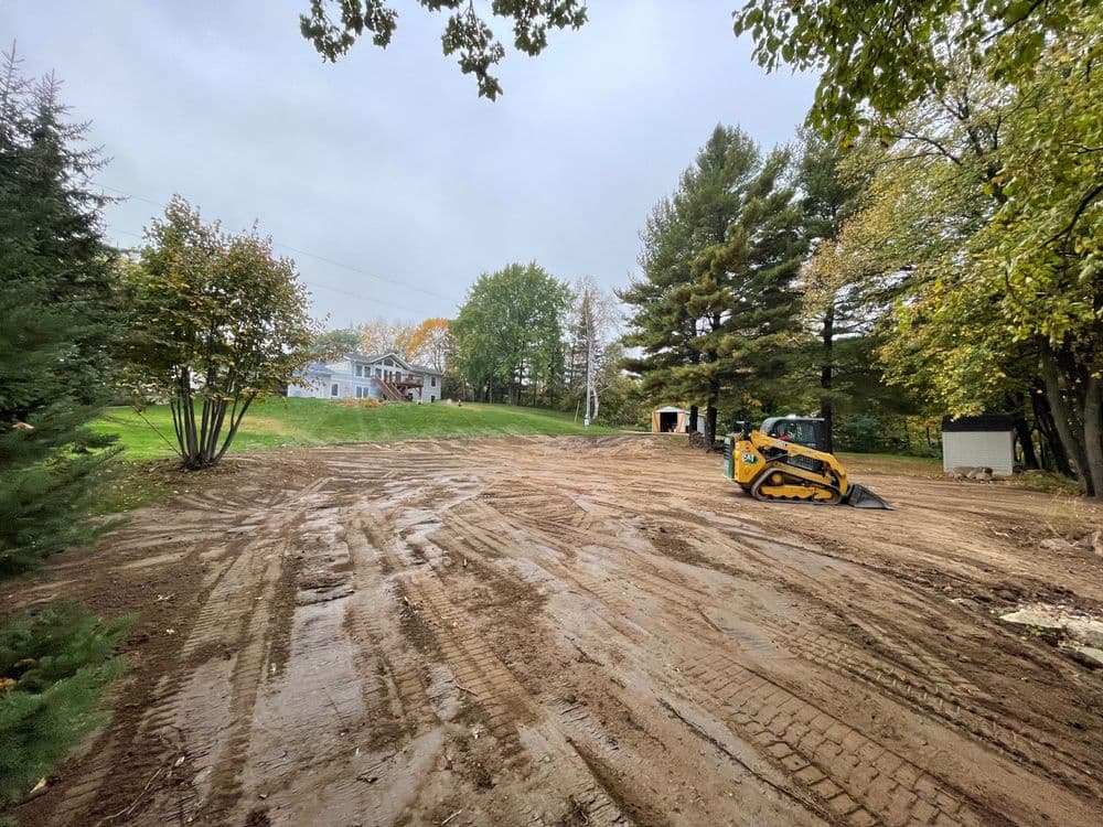 Cleared land with construction equipment and trees in a cloudy environment.