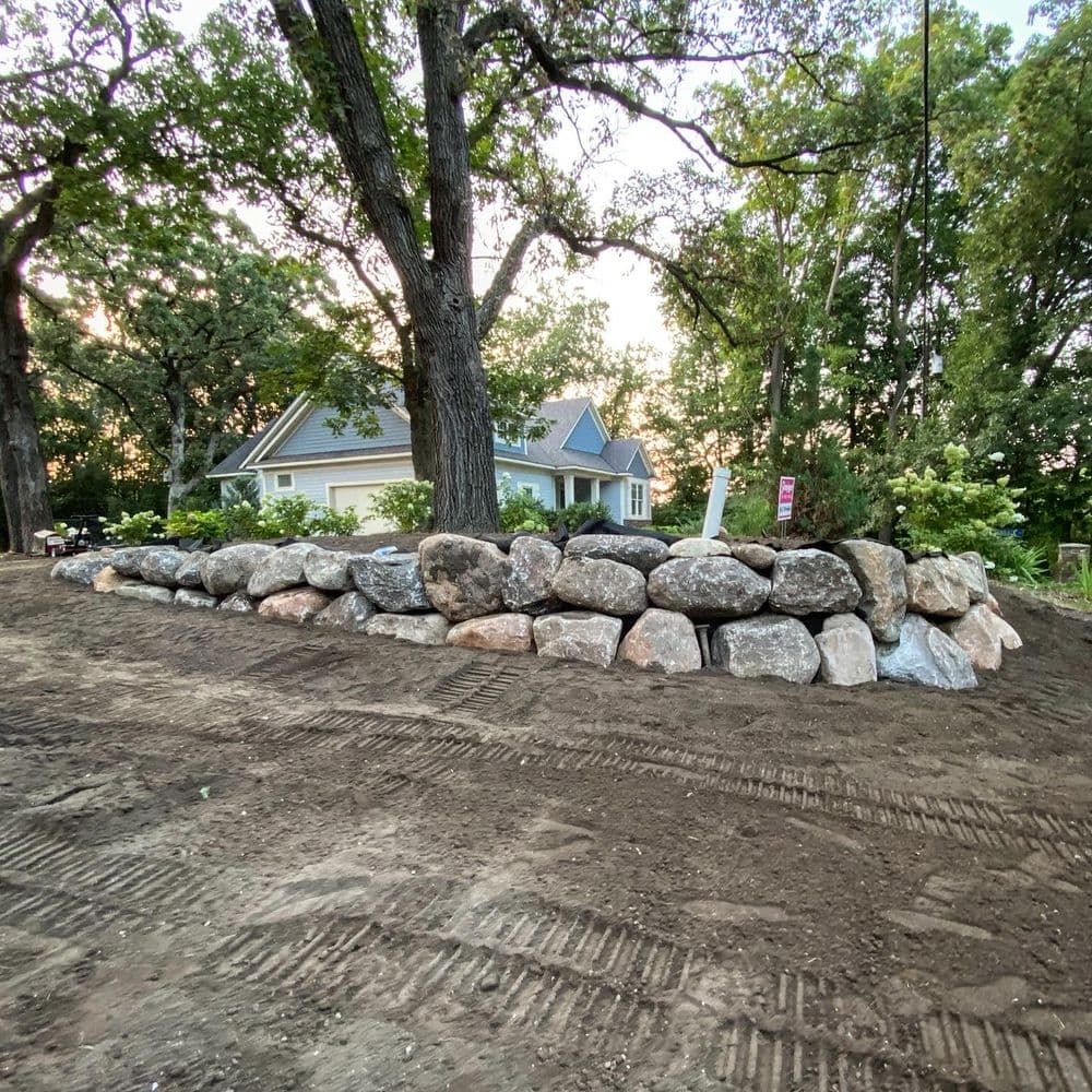 Landscaped yard featuring a stone wall, surrounded by trees and a home in the background.