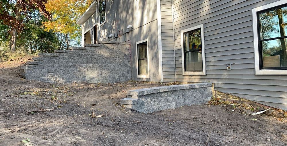 Newly built stone steps leading to a modern home with gray siding and landscaping.