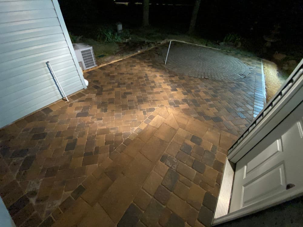 Illuminated patio with decorative paver stones viewed from an open doorway at night.