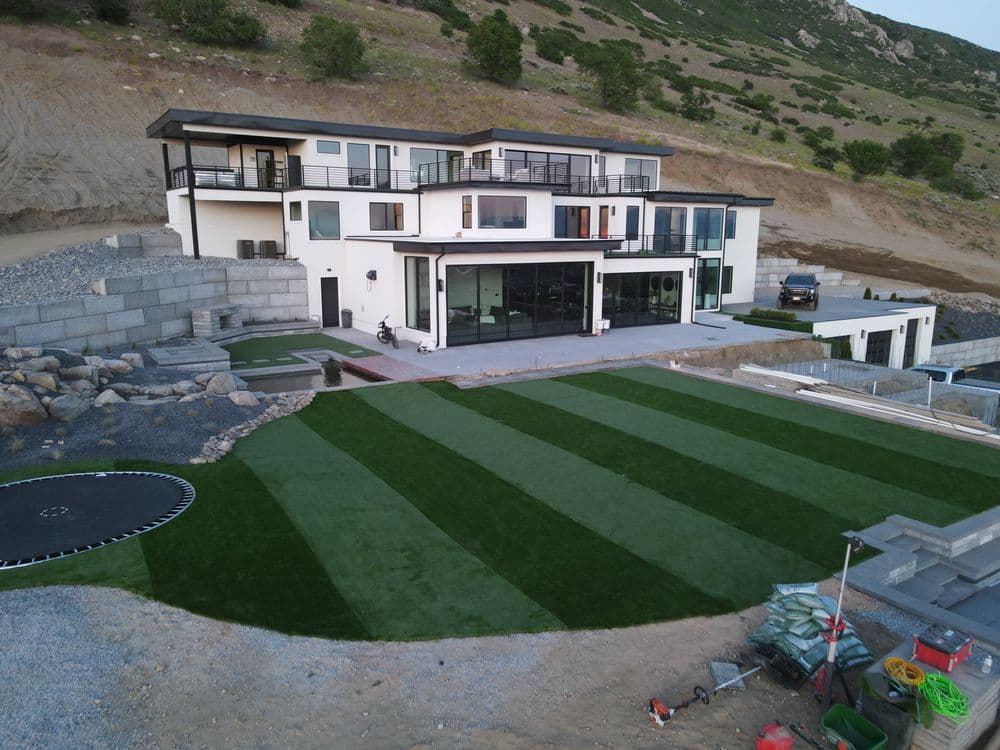 Modern house with large glass windows, surrounded by landscaped green lawn and rocky terrain.