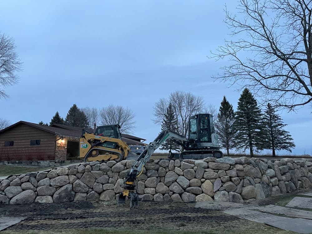 Excavation equipment on a stone wall at a residential property during twilight.