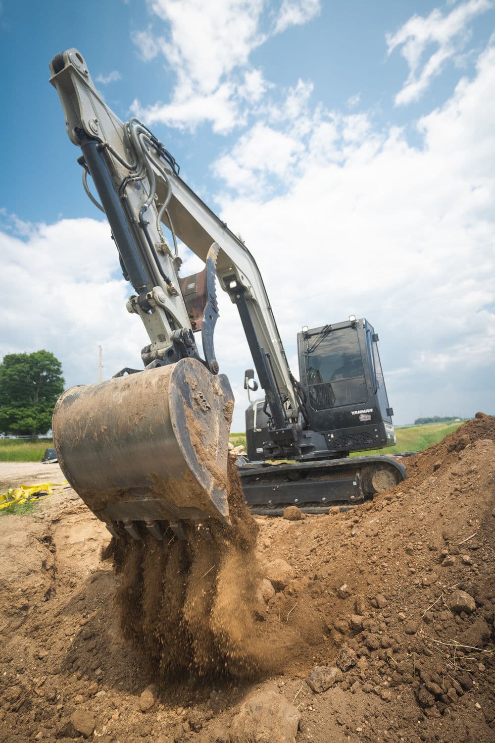 Excavator digging soil at a construction site under a blue sky.