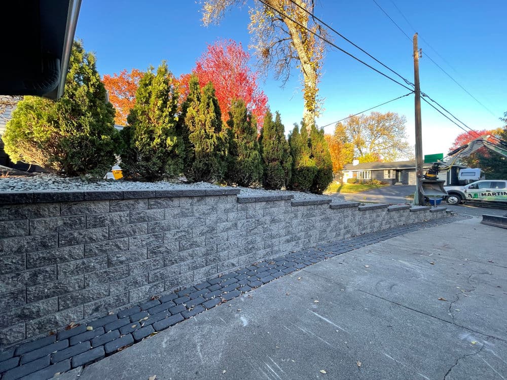 Decorative stone wall and landscaped yard with autumn foliage and blue sky.