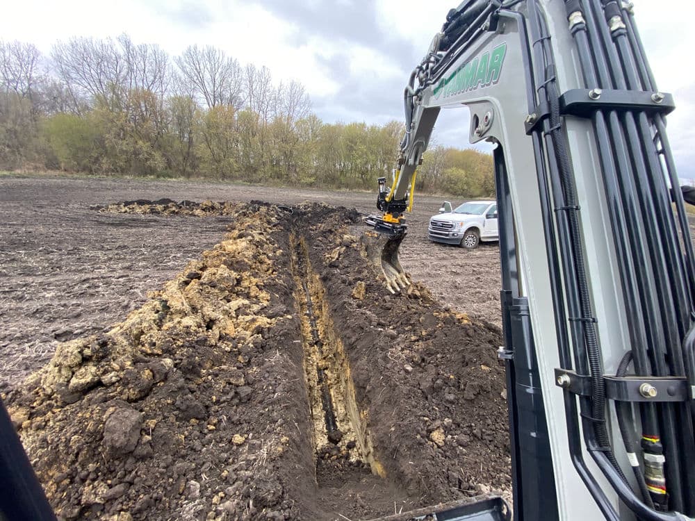 Excavator digging earth on a construction site with trees in the background.