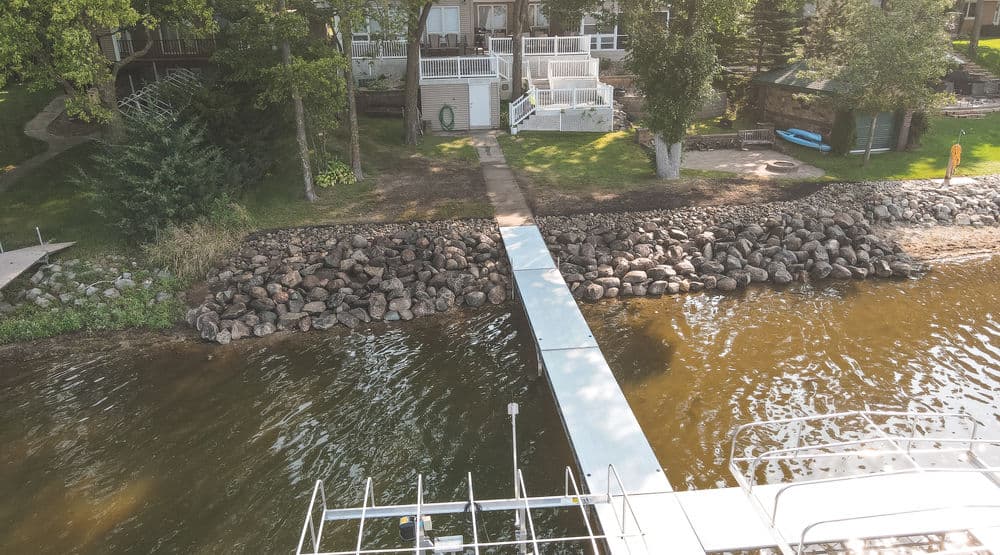 Dock leading to a calm lake surrounded by trees and a shoreline of rocks.