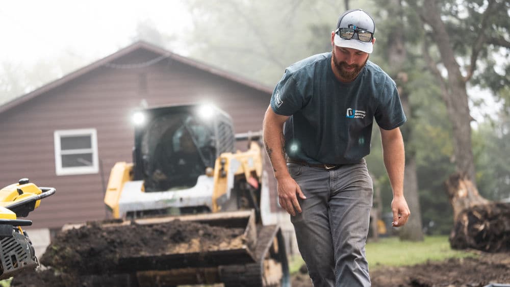 Construction worker in a teal shirt walking on a job site near heavy machinery.