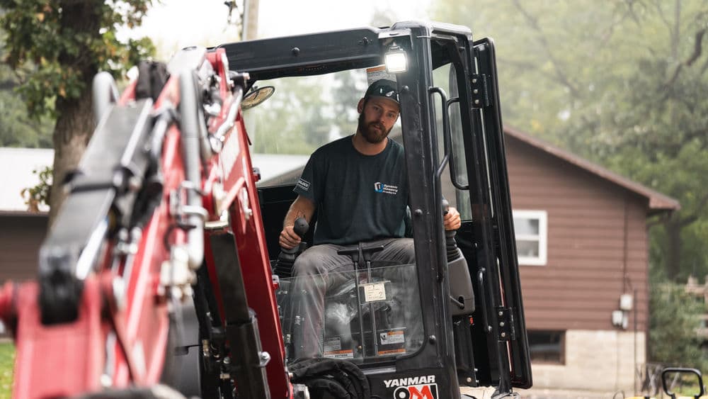 Man operating a Yanmar construction vehicle in a residential area.