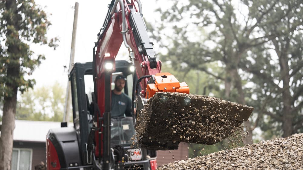Excavator operator loading gravel from a pile for landscaping project outdoors.