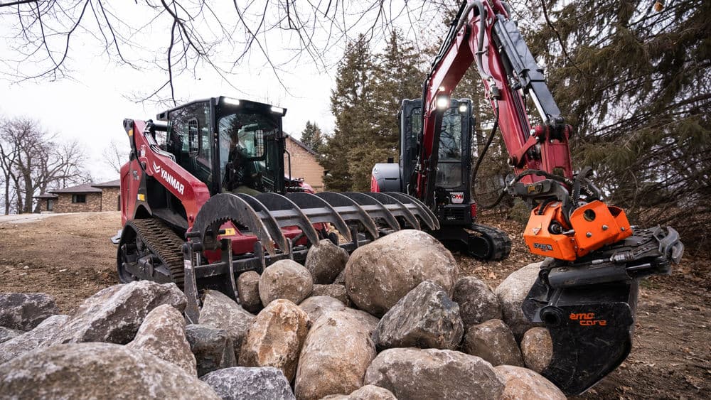 Heavy machinery working on landscaping with rocks in a residential area.