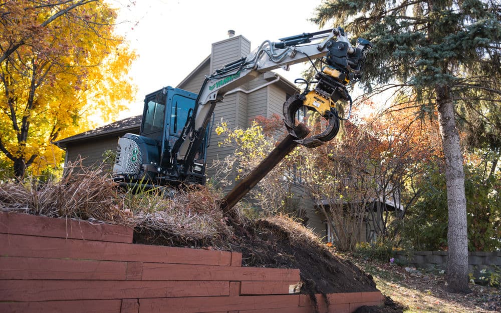 Excavator removing a wooden post in a residential yard during autumn.