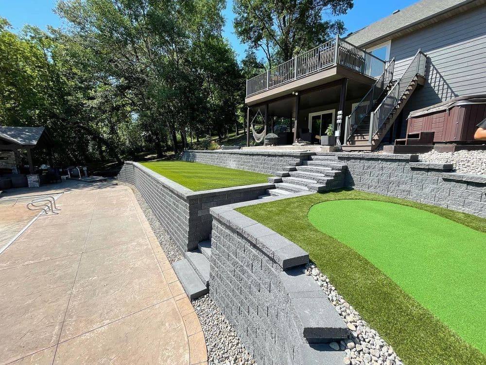 Landscaped backyard featuring multi-level stone terraces, synthetic turf, and a deck.