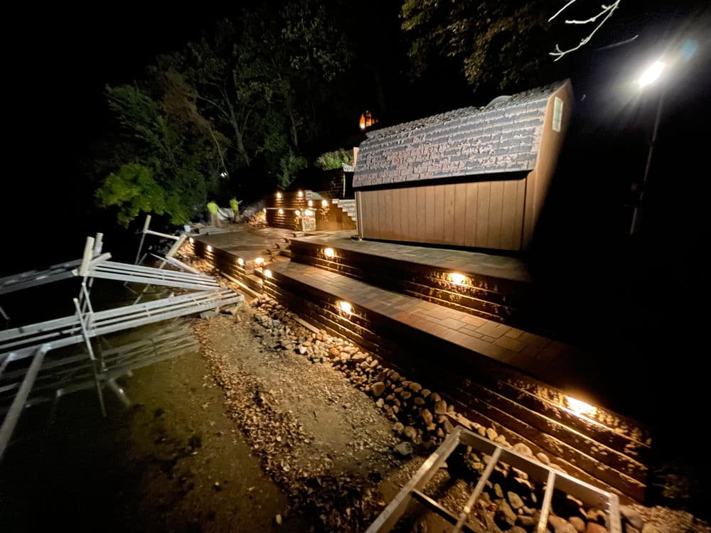 Nighttime view of a lit pathway leading to a wooden shed by a lake.