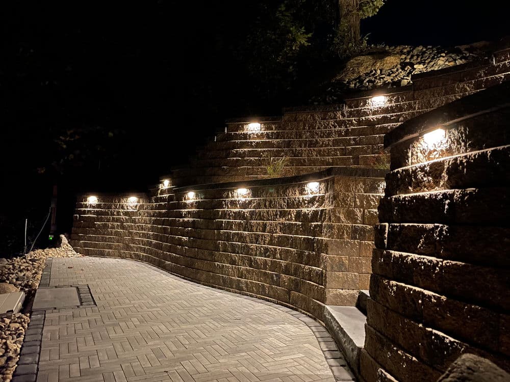 Illuminated stone pathway with stairs and landscaping at night.