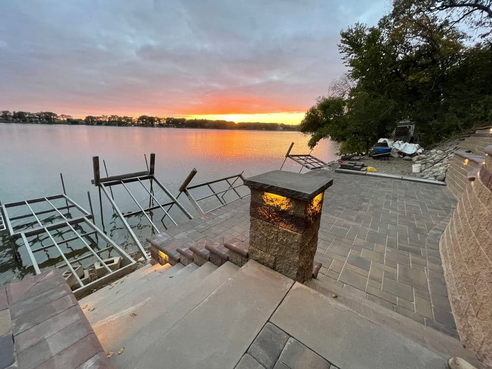 Scenic lakeside view at sunset with stone patio and boat docks.