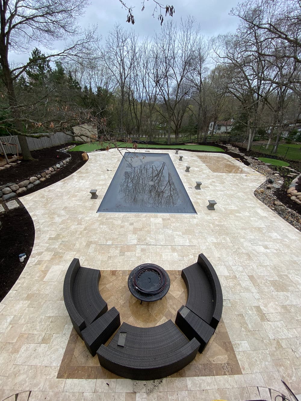 Aerial view of a modern pool with stone patio and circular seating area surrounded by trees.