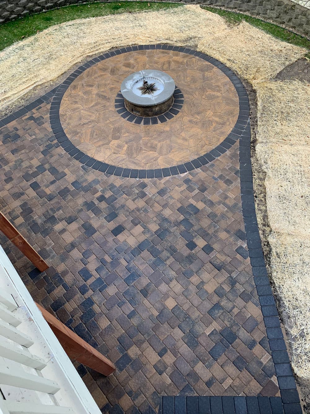 Paved outdoor patio with circular fire pit, surrounded by neatly arranged bricks.