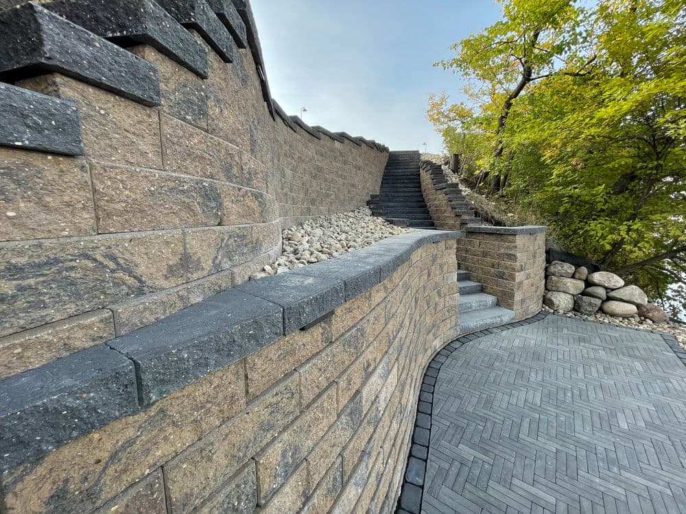 Curved stone wall leading to a staircase amid greenery and landscaped stones.