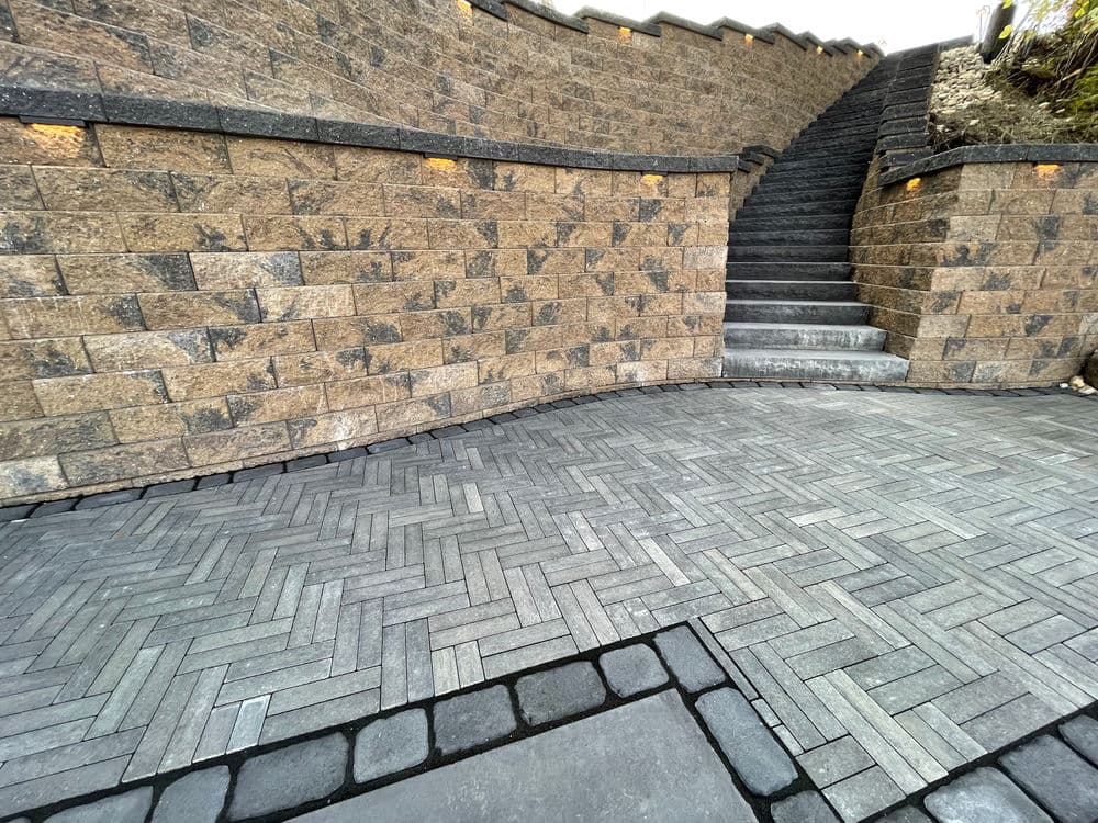 Curved stone wall with steps and patterned paver walkway in a landscaped area.