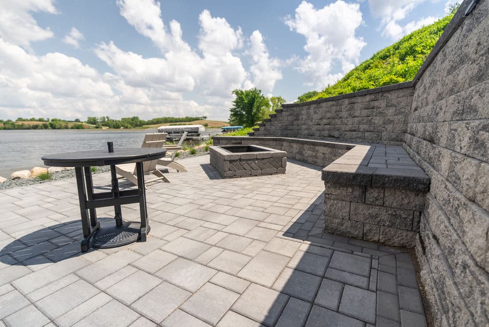 Outdoor patio by the river featuring stone seating, fire pit, and table with chairs.