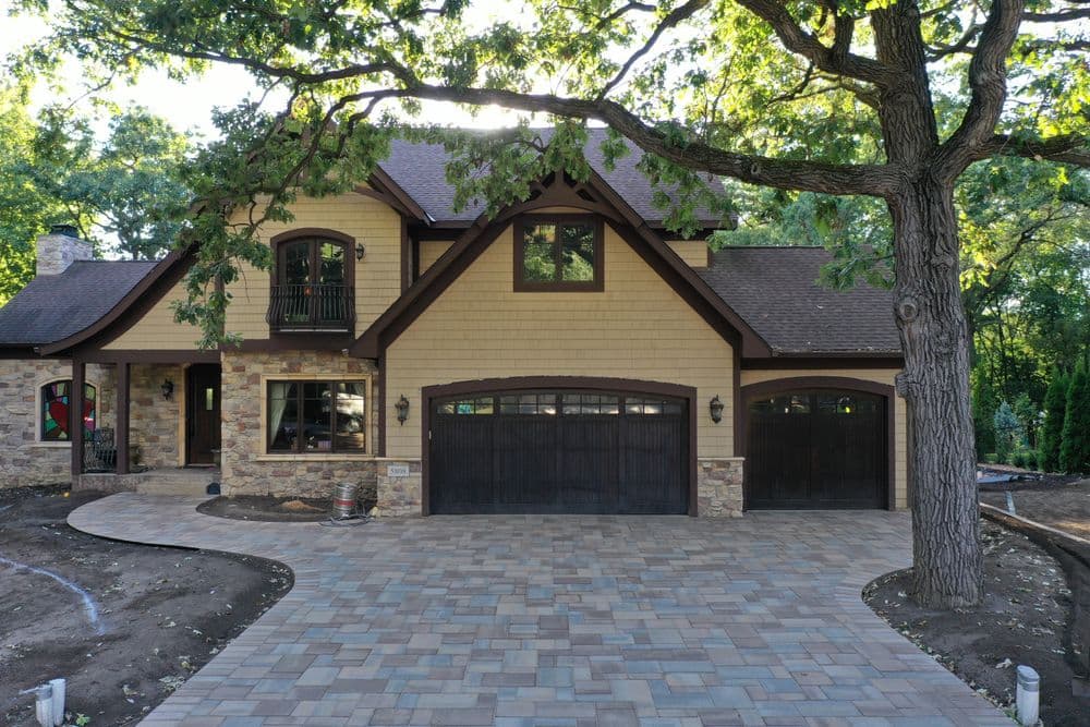 Modern two-story house with stone accents, large driveway, and surrounding trees.