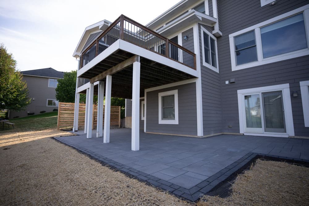 Modern backyard patio with a raised deck and sleek paver flooring, surrounded by greenery.
