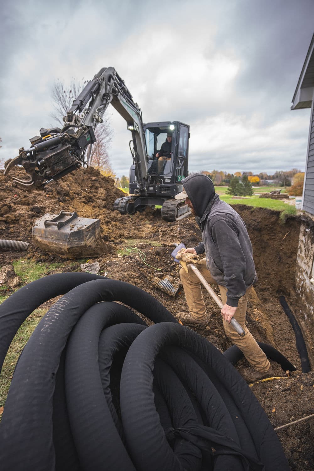 Construction workers operating machinery for excavation, with large pipes visible nearby.