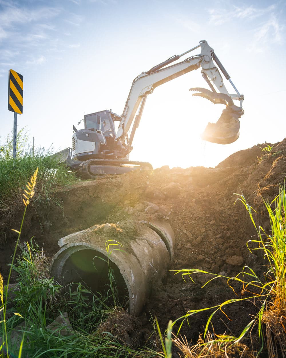 Excavator digging near a concrete pipe in a sunny construction site.