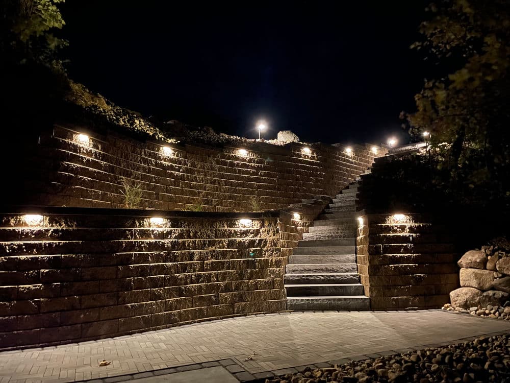 Illuminated stone staircase in a landscaped garden at night.