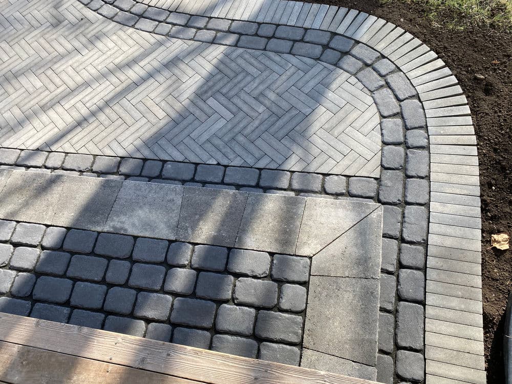 Paved pathway featuring herringbone and cobblestone patterns in a landscaped area.