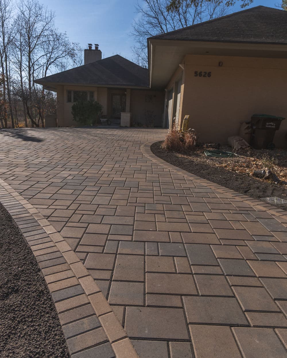 Paved driveway with curved design leading to a residential home in a sunny outdoor setting.