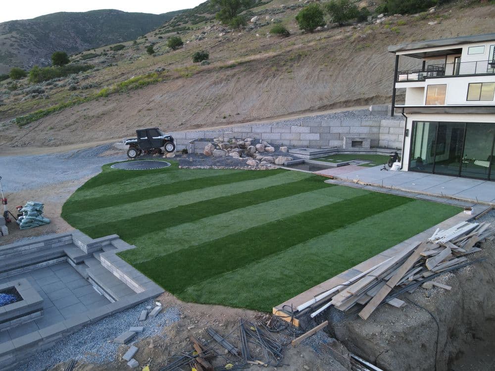 Modern home with lush green lawn, patio area, and rocky landscaping in a hillside setting.