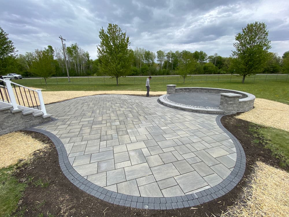 Beautifully paved patio with circular stone feature and landscaping under a cloudy sky.