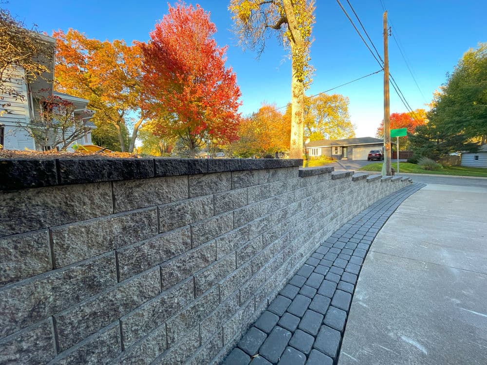 Curved stone wall with autumn trees and a clear blue sky in the background.