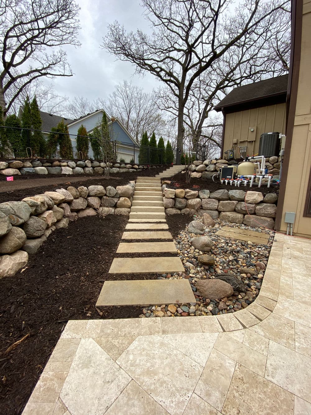 Landscaped garden with stone path, retaining walls, and trees in a suburban setting.