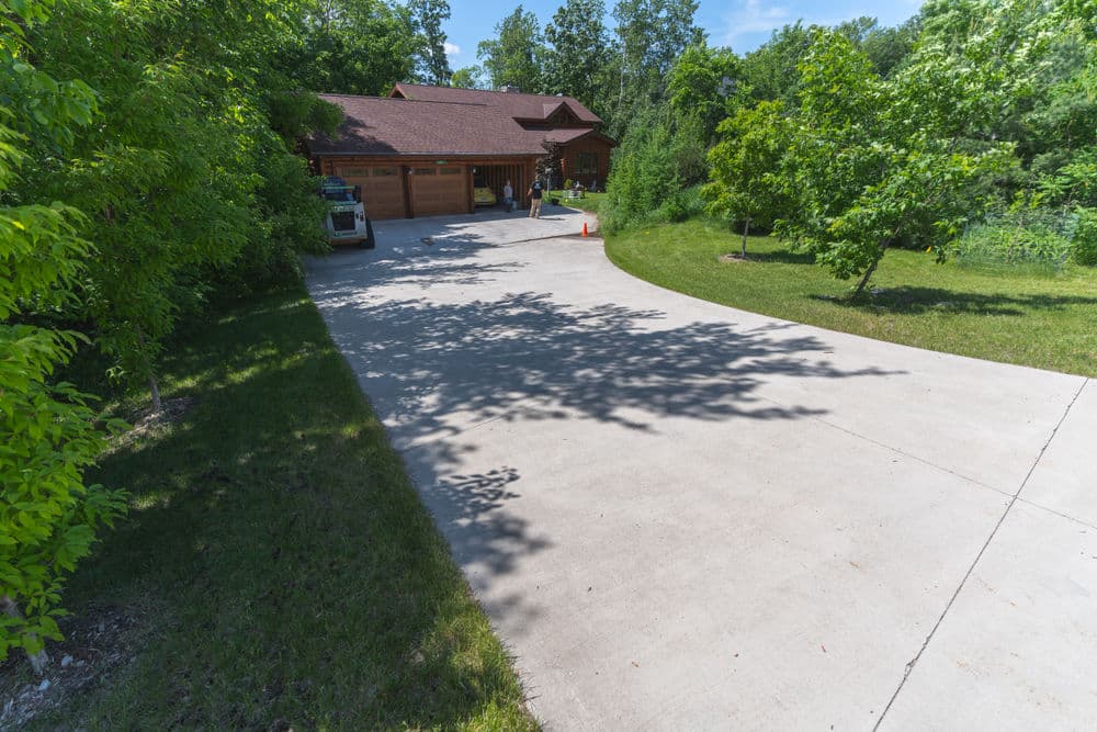 Driveway leading to a cabin surrounded by trees under a clear blue sky.