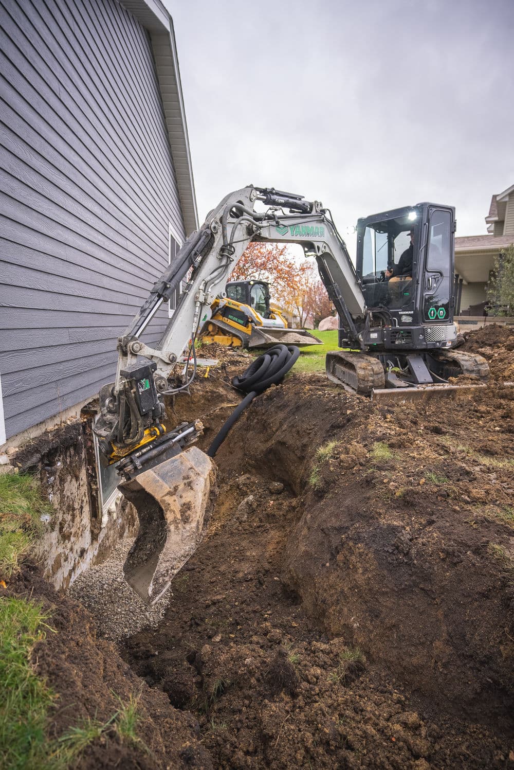 Excavator digging a trench next to a house for utility installation.