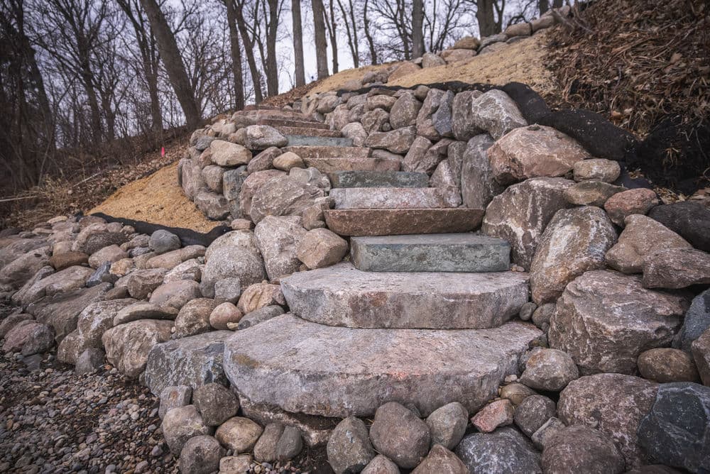 Stone steps leading up a hillside, surrounded by large rocks and barren trees.